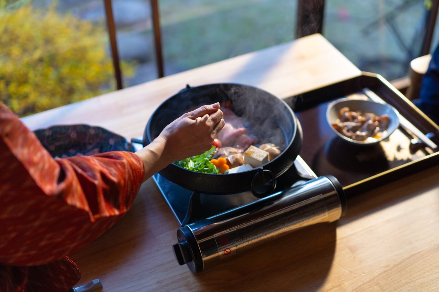 日本庭園を望むSashoの窓辺で、着物姿のスタッフがすき焼きを調理する様子
