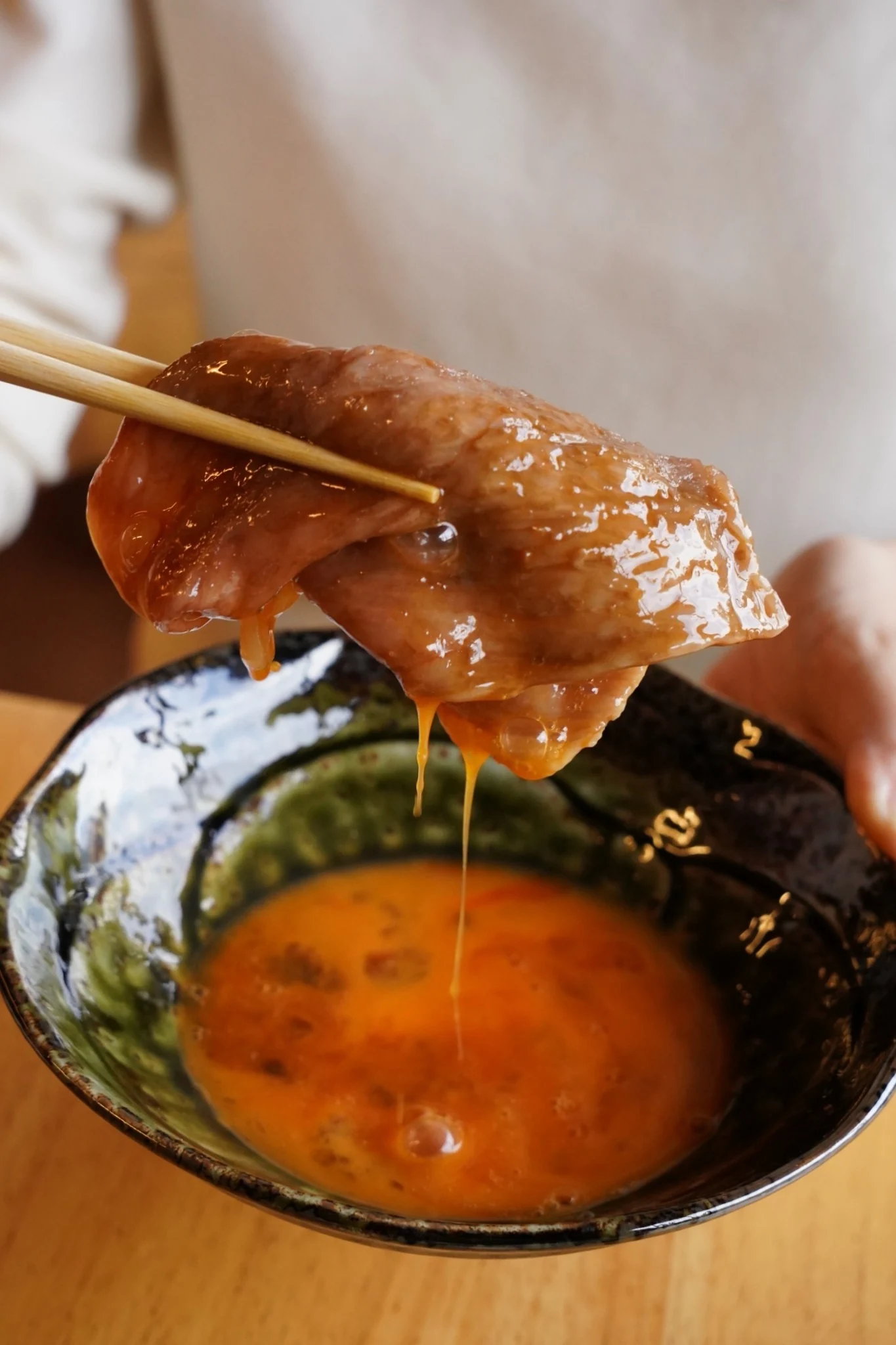 溶き卵をまとわせたすき焼きの牛肉を箸で持ち上げる様子