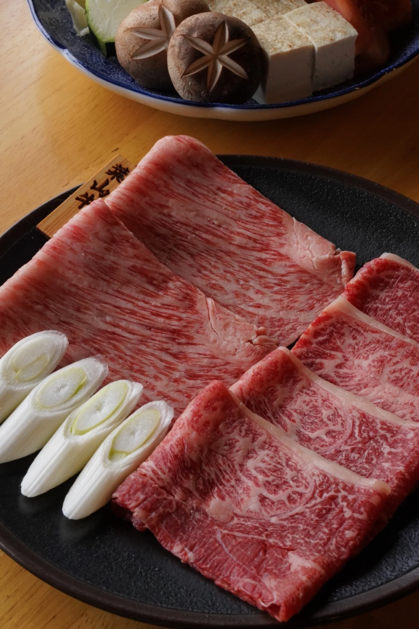 黒い皿に盛り付けられた霜降りの和牛とねぎ